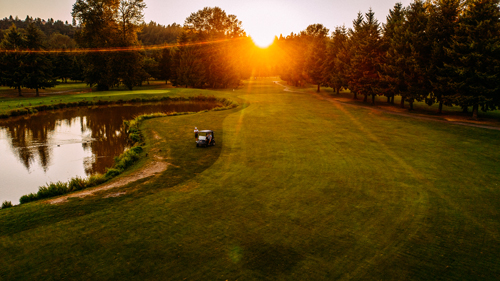 A sunset descends behind the trees at the Riverbend Golf Course, casting an orange glow.