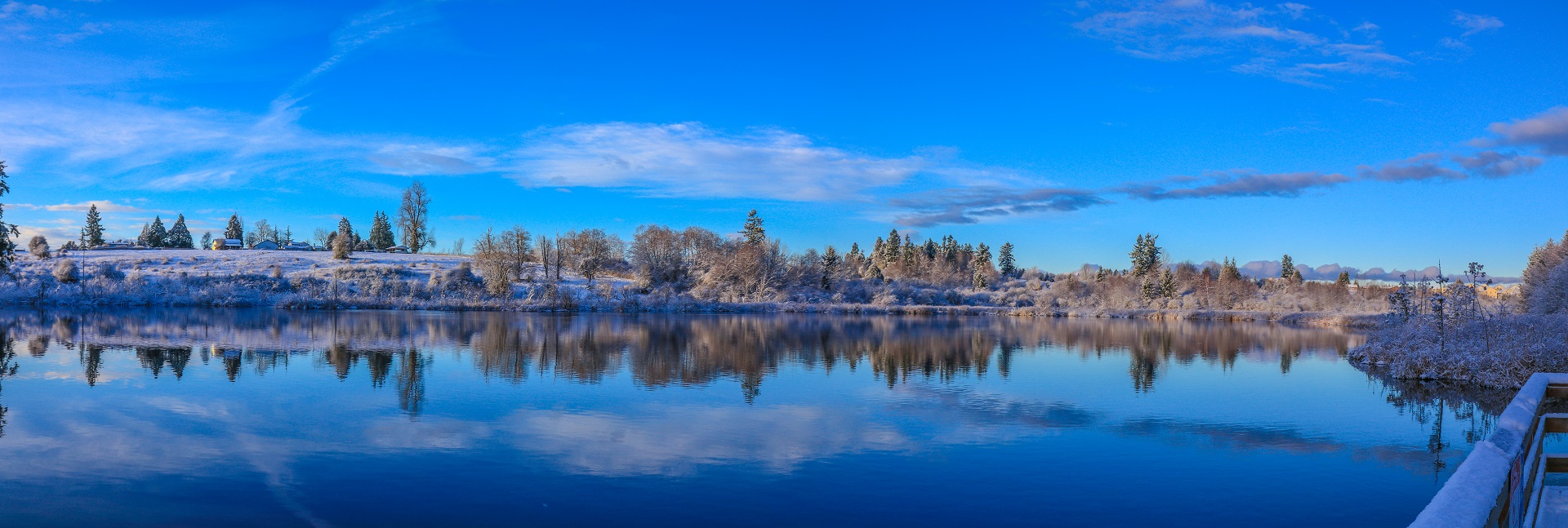 Snowy slope with trees and clear blue winter sky reflected in Clark Lake