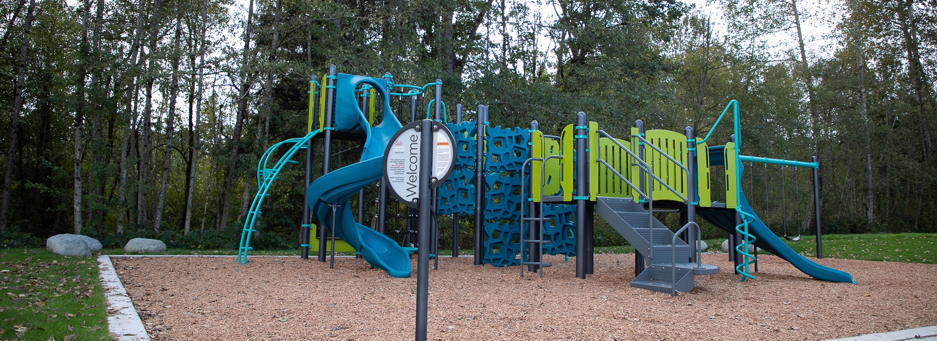 Blue and green play structure with spiral slide and climbing elements in a park