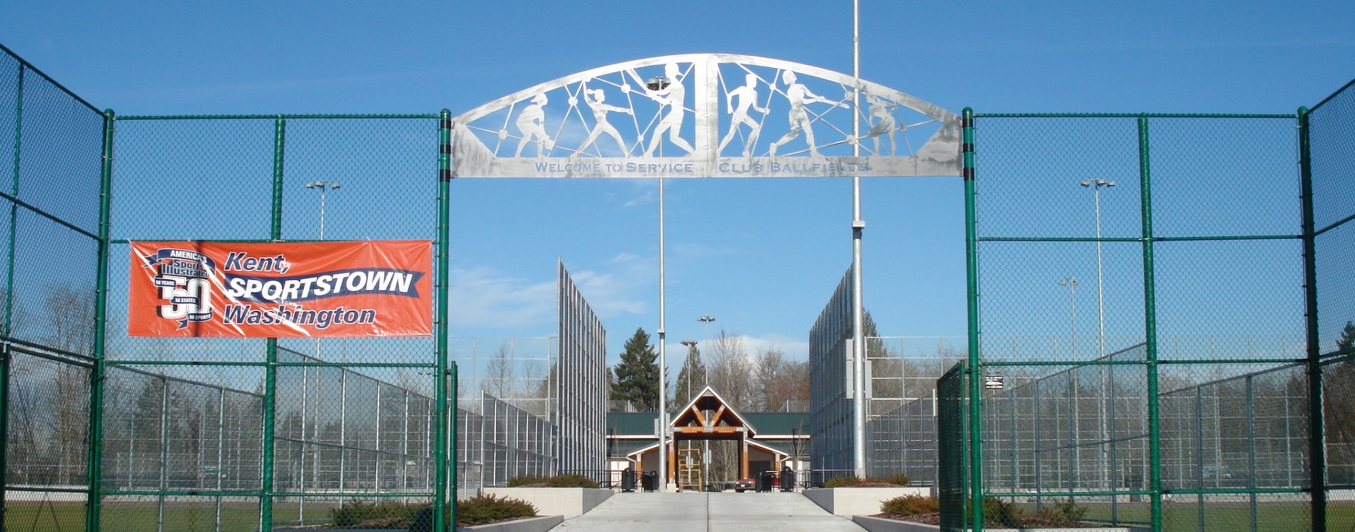 Baseball player-shaped cutouts in a decorative metal, arched panel over a park entry sidewalk