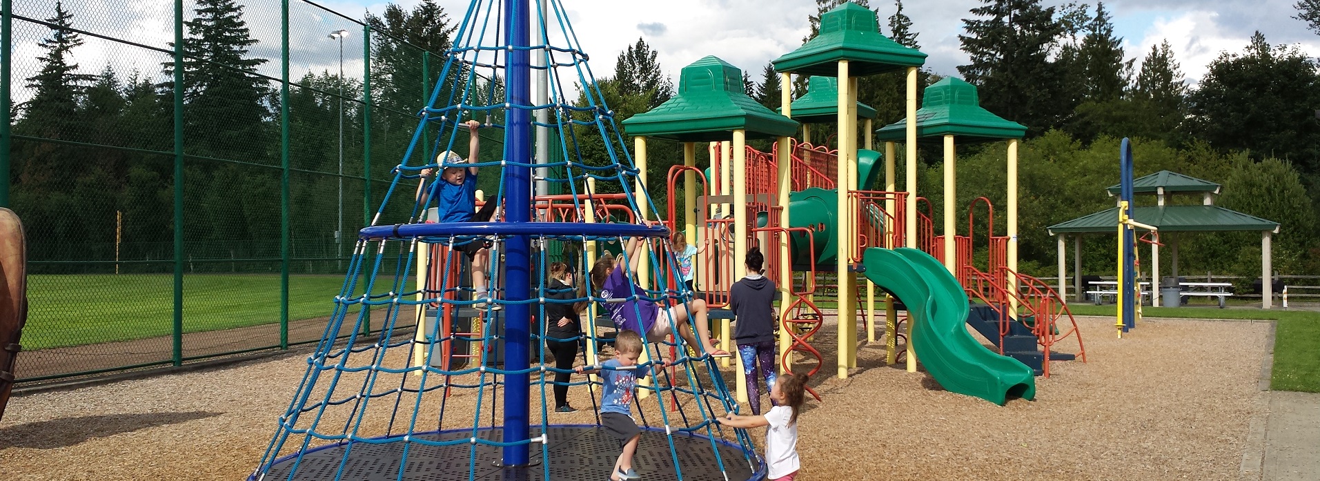 Blue conical climbing structure with children on it near a play structure with a green slide