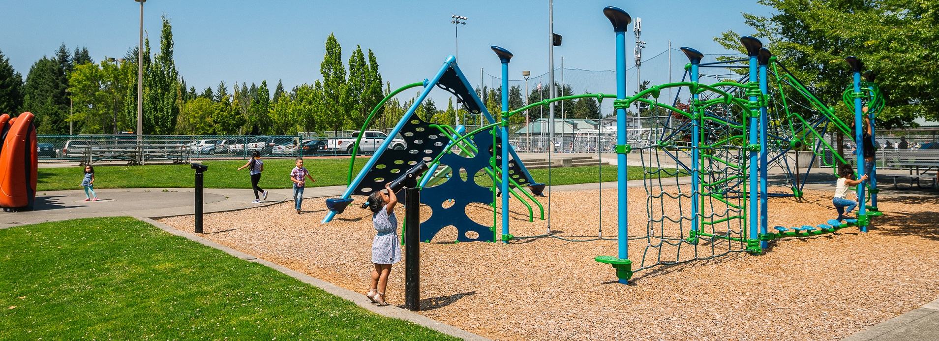 Blue and green play structure with children climbing on it on a sunny day