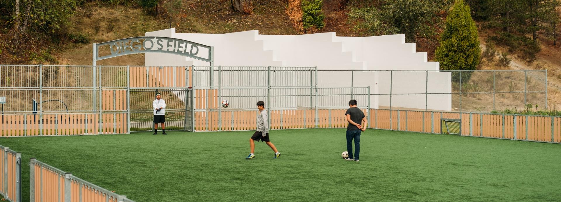 Diego's Field Multi-Use Games Area enclosure and 3 people practicing with soccer balls